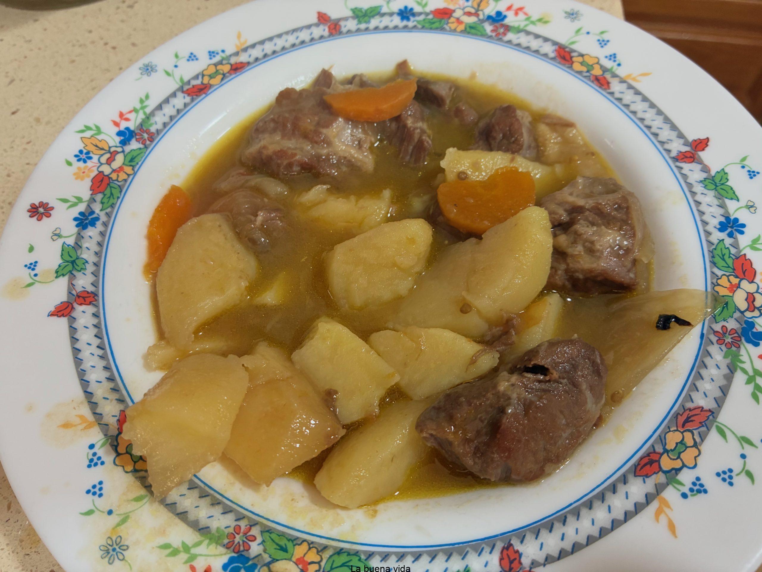 Plato de estofado de carrillera de ternera con trozos de patata cocida y zanahoria en salsa.