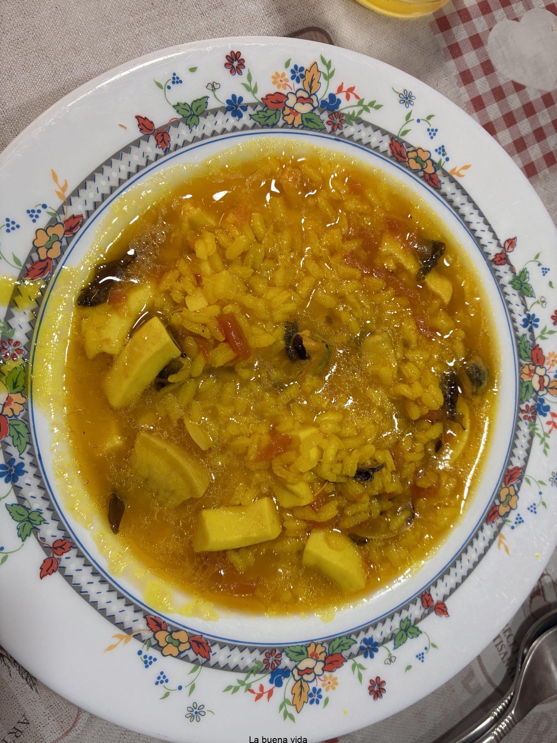 Plato de sopa de arroz caldoso de color amarillo intenso, cocinado con caldo de pescado, trozos de calamar, mejillones y almejas.